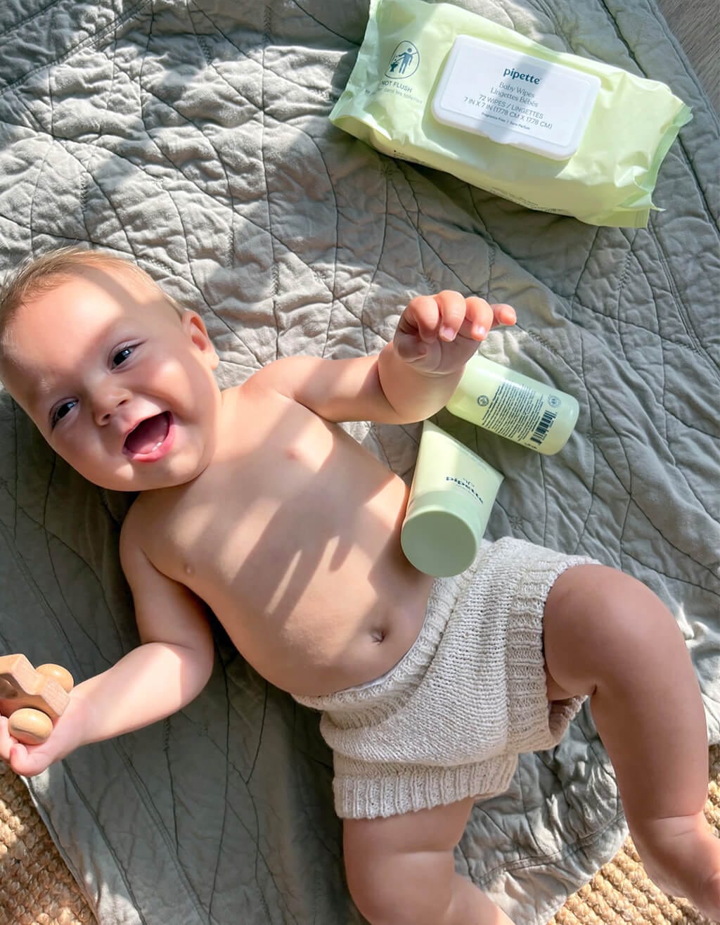 Baby Laying Down on Bed with bestselling Pipette SPF, Baby Oil & Baby Wipes.